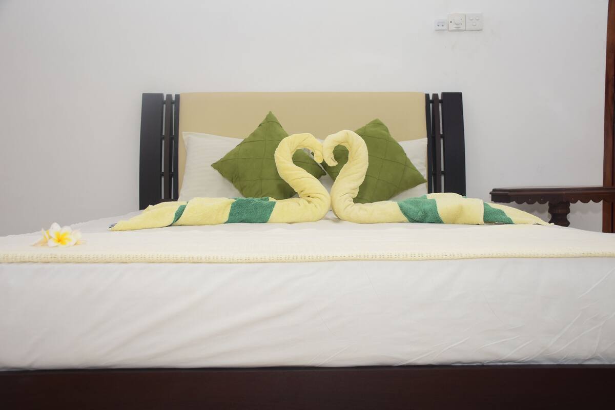 A neatly made bed with a heart-shaped towel arrangement and a single flower on the bed.
