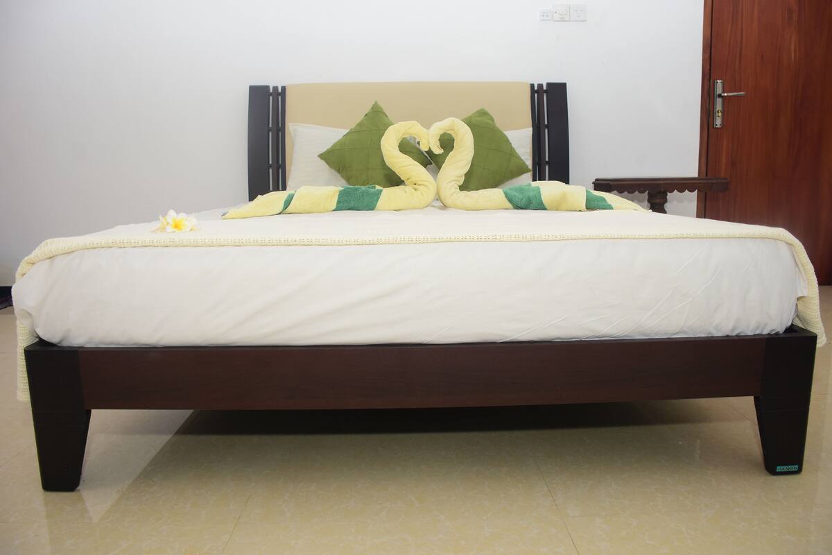 A neatly made bed with a heart-shaped pillow arrangement and a single flower on the bed.