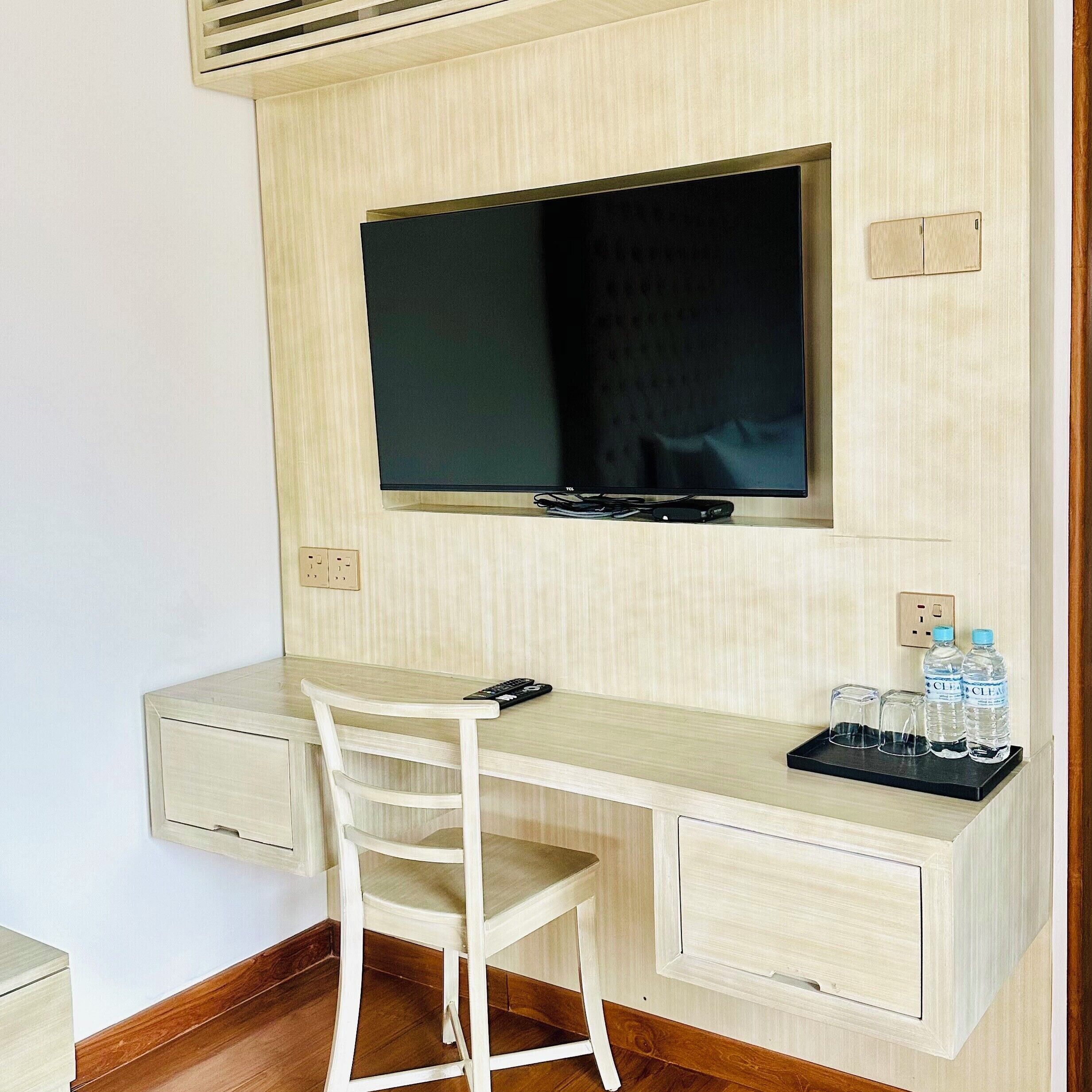Ein kleiner, privater Arbeitsraum mit Schreibtisch, Stuhl, Fernseher und einer Wasserflasche.