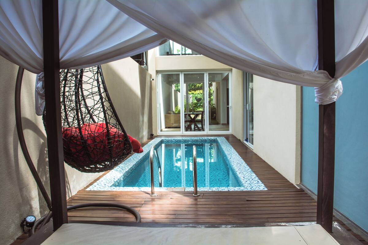 A pool area with a hanging chair, a wooden deck, and a glass door leading to an outdoor space.