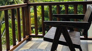 A balcony with a wooden table and chairs, surrounded by a wooden railing, overlooking a lush green landscape and a building in the background. - Kings Landing Unawatuna (Unawatuna)