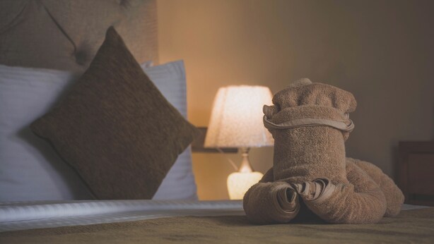 A neatly made bed with a single brown pillow, a rolled-up brown blanket, and a lamp in the background. - Kings Landing Unawatuna (Unawatuna)