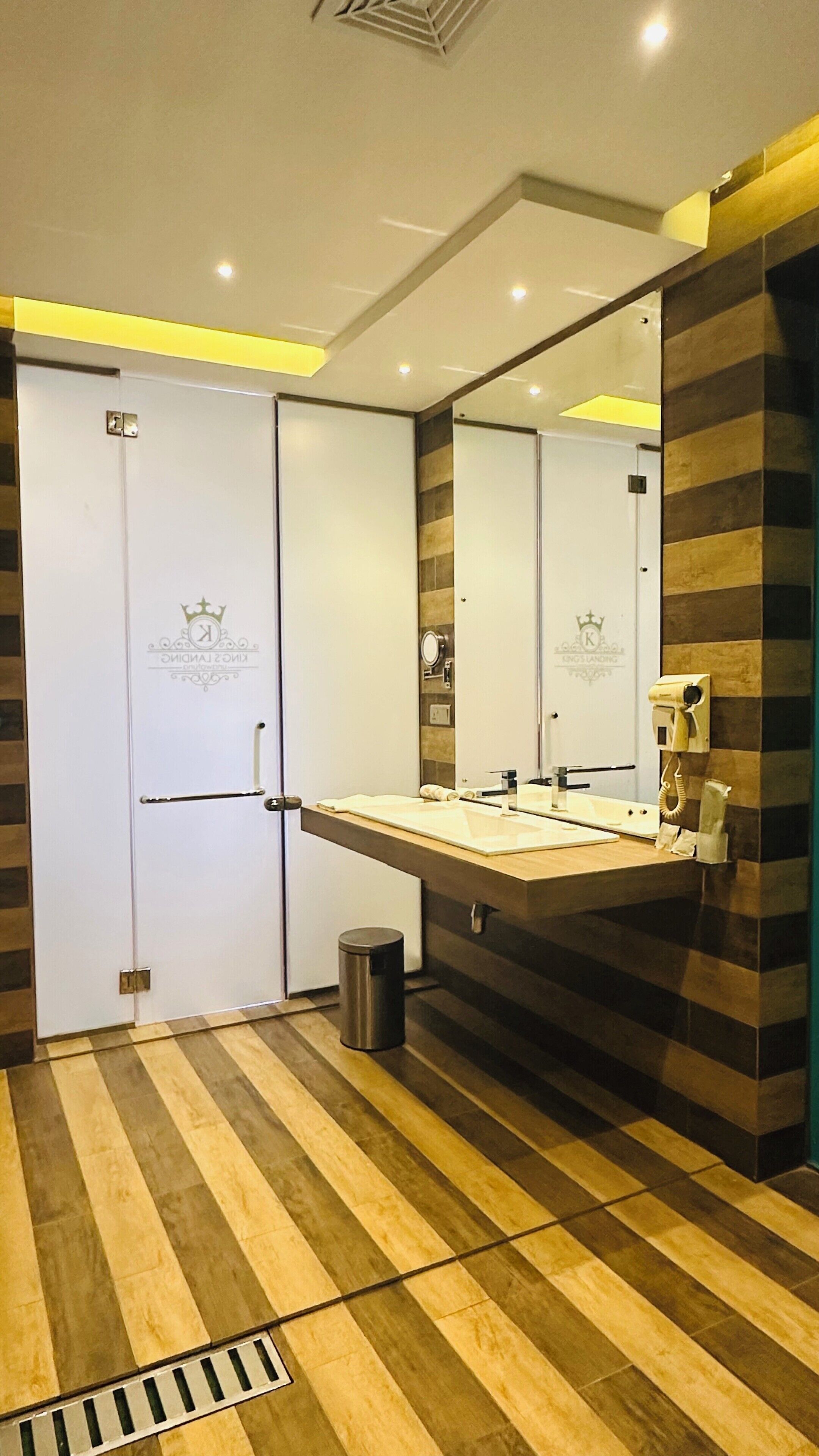 A modern bathroom with a large mirror, a sink, and a trash bin.
