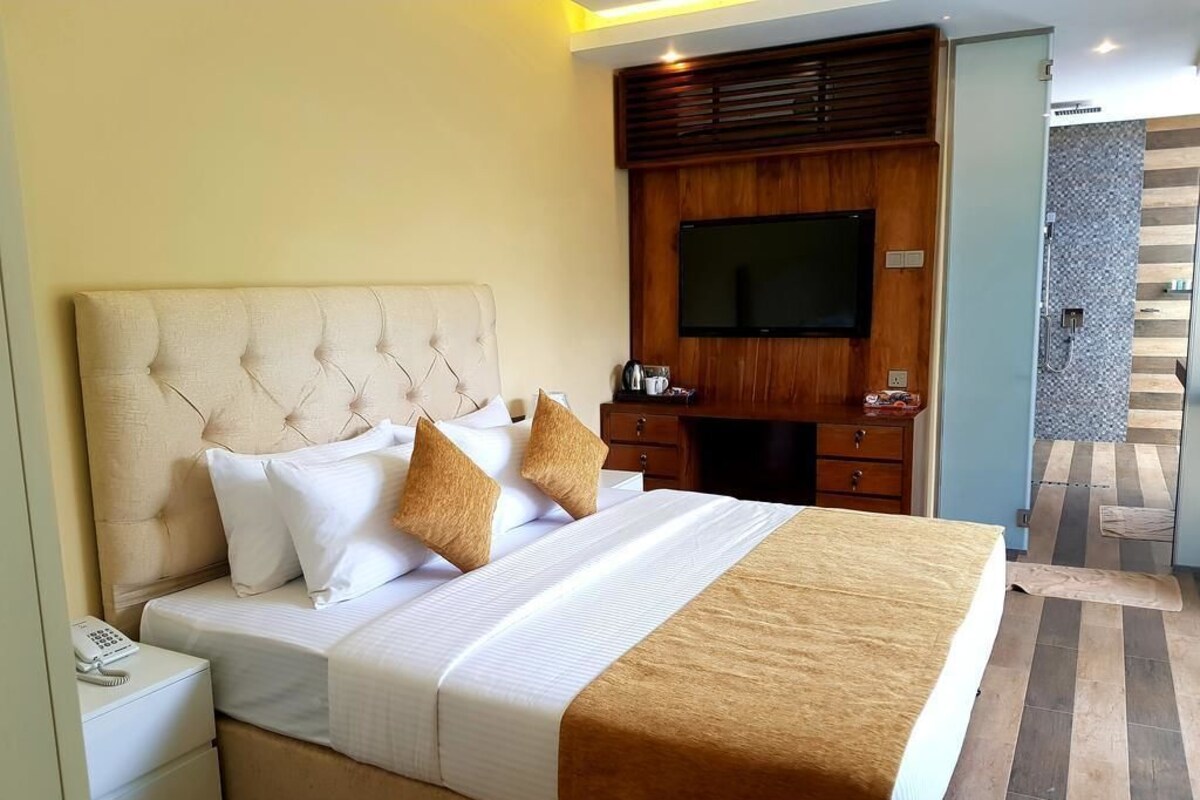 A hotel room with a large bed, a television, a desk, and a shower area.