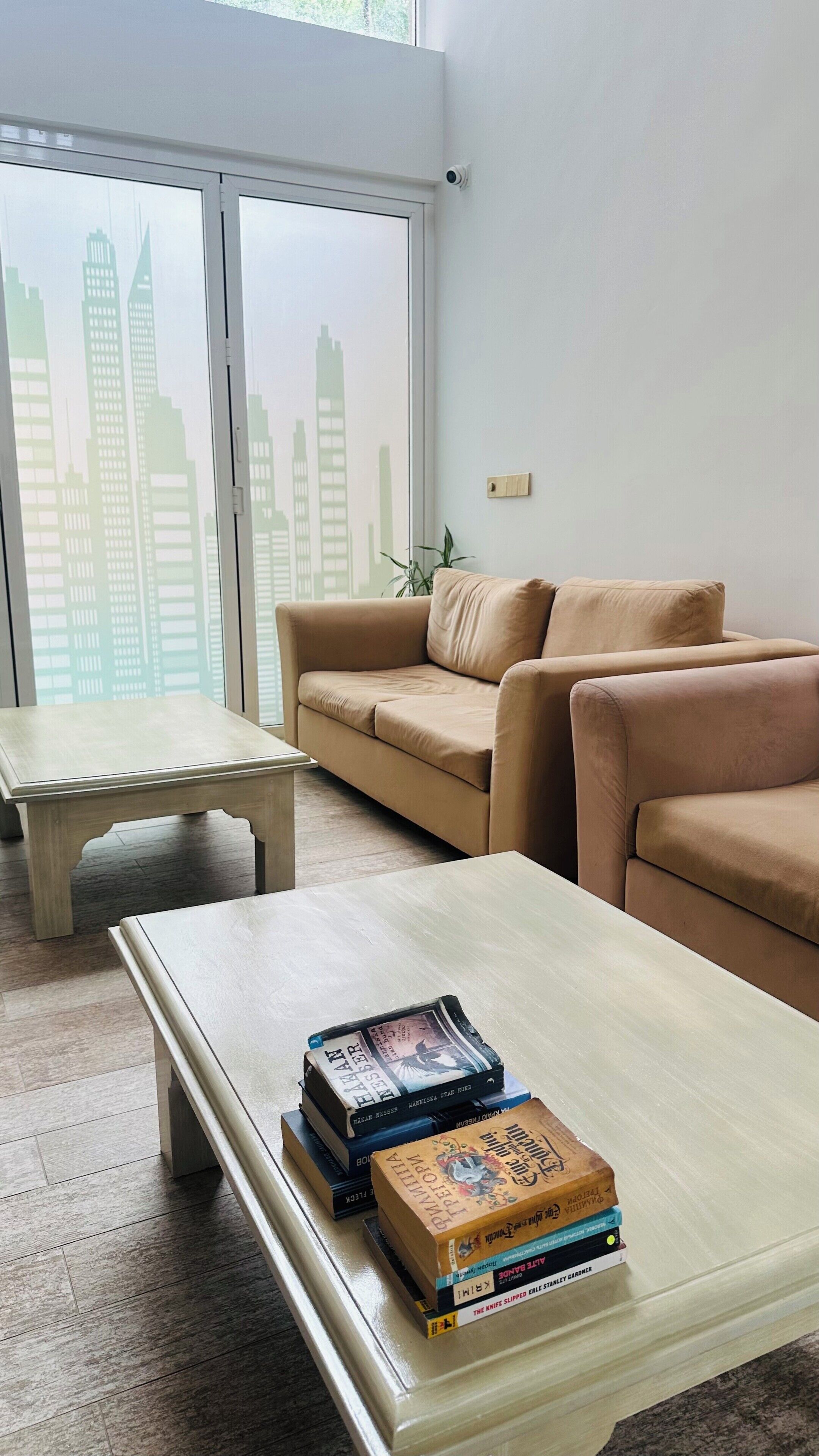 A living room with a sofa, a coffee table, and a view of a cityscape through large windows.