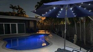 A swimming pool with a curved edge, surrounded by a patio area with chairs and a table. - House - Miami pool house, near Miami Int Airport and attractions. (Miami Springs)