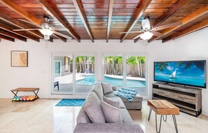 A living room with a gray sofa, wooden coffee table, and a TV on a wooden stand. - House - Miami pool house, near Miami Int Airport and attractions. (Miami Springs)