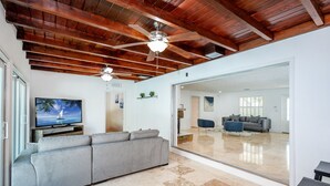 A modern living room with a large gray sectional sofa, a ceiling fan, and a flat-screen TV on a wooden stand. - House - Miami pool house, near Miami Int Airport and attractions. (Miami Springs)
