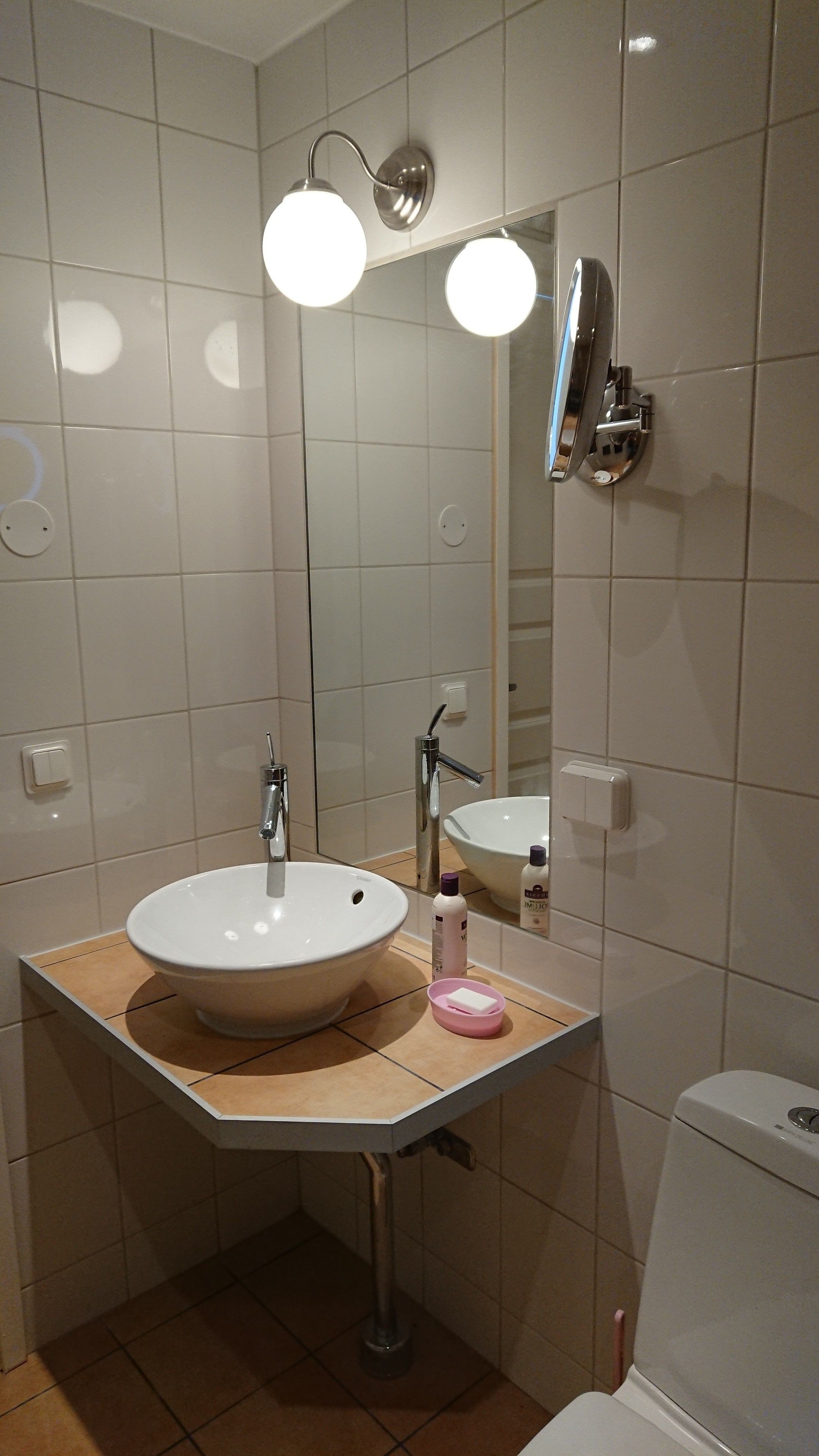 Kylpyhuone, jossa on valkoinen pesuallas, peili, käsisuihku ja wc-istuin.