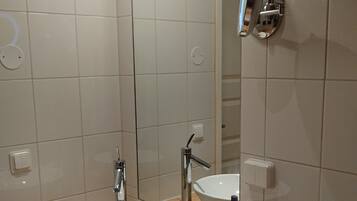 Kylpyhuone, jossa on valkoinen pesuallas, peili, käsisuihku ja wc-istuin.