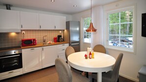A modern kitchen with white cabinets, a stainless steel refrigerator, a red microwave, and a round dining table with chairs.