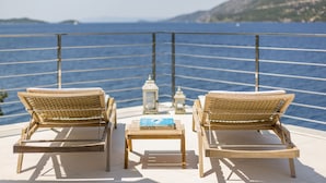 Due poltrone in vimini rivolte verso un balcone con vista sul mare e colline lontane.