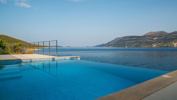 Una piscina con vista libera sul mare e colline in lontananza.