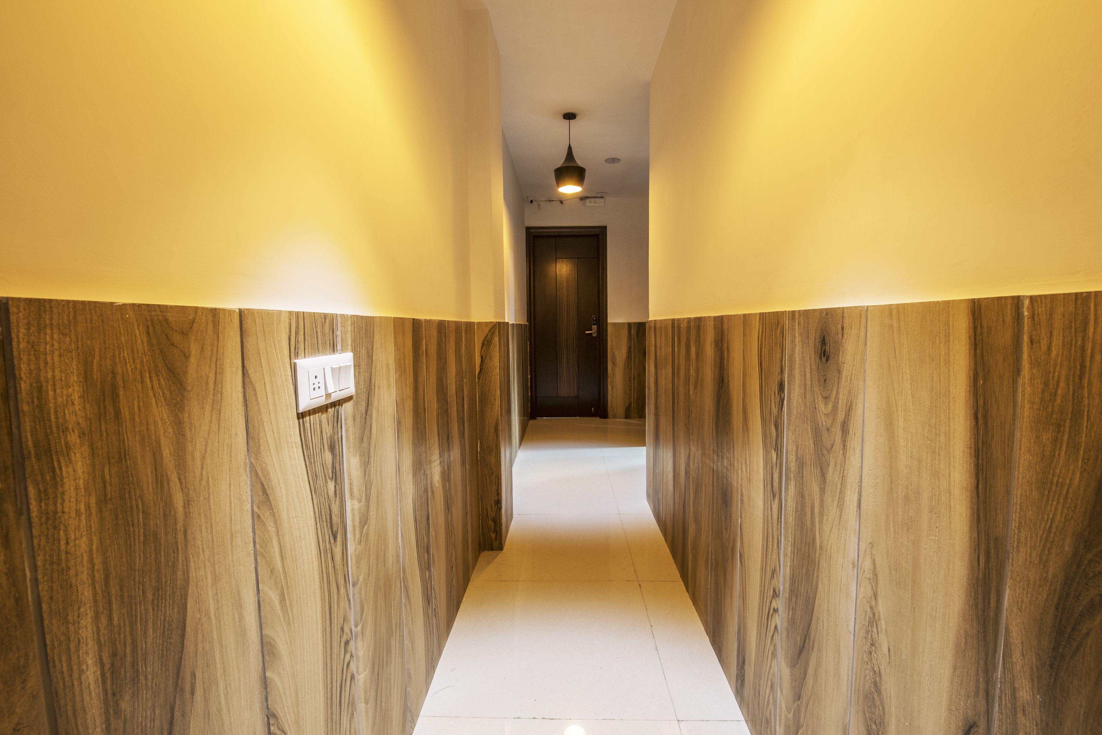A hallway with wooden paneling and a white floor, leading to a door at the end.