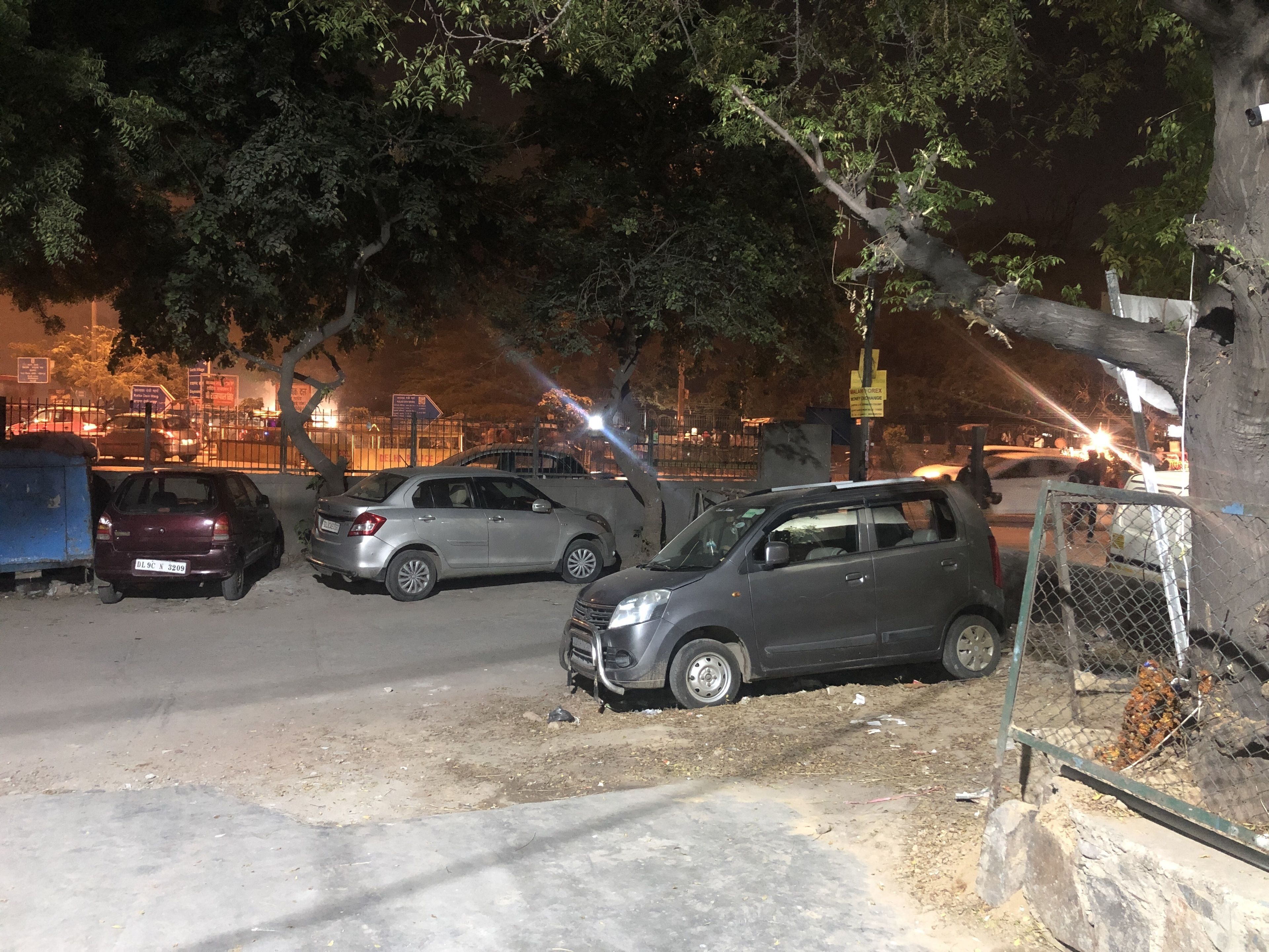 Un espace de stationnement avec plusieurs voitures, un arbre et une clôture en treillis métallique.