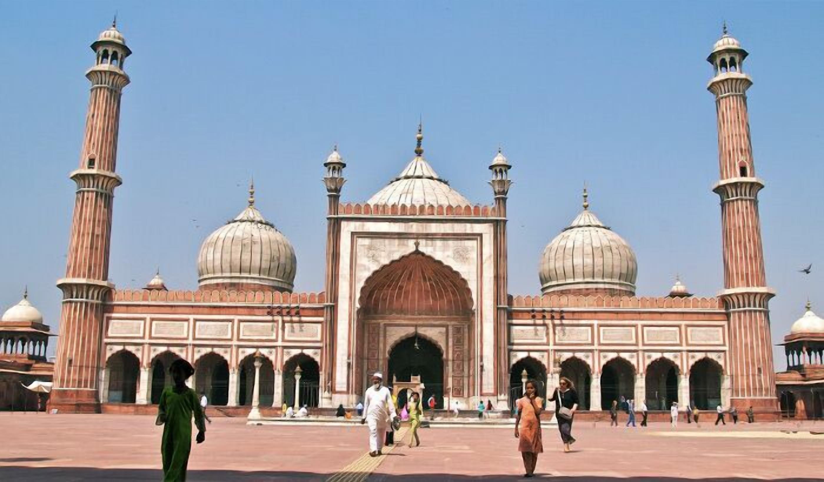 Un grand bâtiment historique doté de plusieurs dômes et de minarets, avec une entrée en arc de cercle et une vaste cour.
