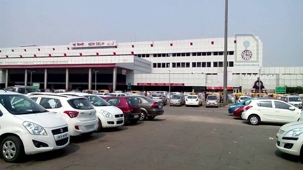 A parking lot with multiple cars parked in front of a building with a clock and signage indicating it is New Delhi.