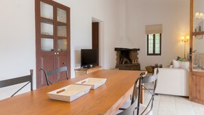 A dining area with a wooden table, chairs, and a television. There is a fireplace with a stone surround and a window with a view. - Typical Ibizan country house with private pool in a beautiful protected environment! (ISLAS BALEARES)