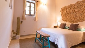 A bedroom with a bed, a nightstand, a lamp, a window with curtains, a cactus, and a stone wall. - Typical Ibizan country house with private pool in a beautiful protected environment! (ISLAS BALEARES)