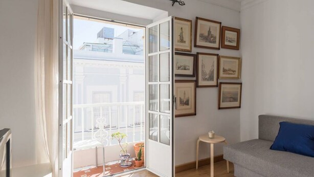 A room with a balcony, a grey sofa, a small table, and framed pictures on the wall. - La Galeria de San Antonio (Cádiz)