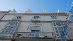A multi-story building with balconies, a central entrance, and a clear sky. - La Galeria de San Antonio (Cádiz)