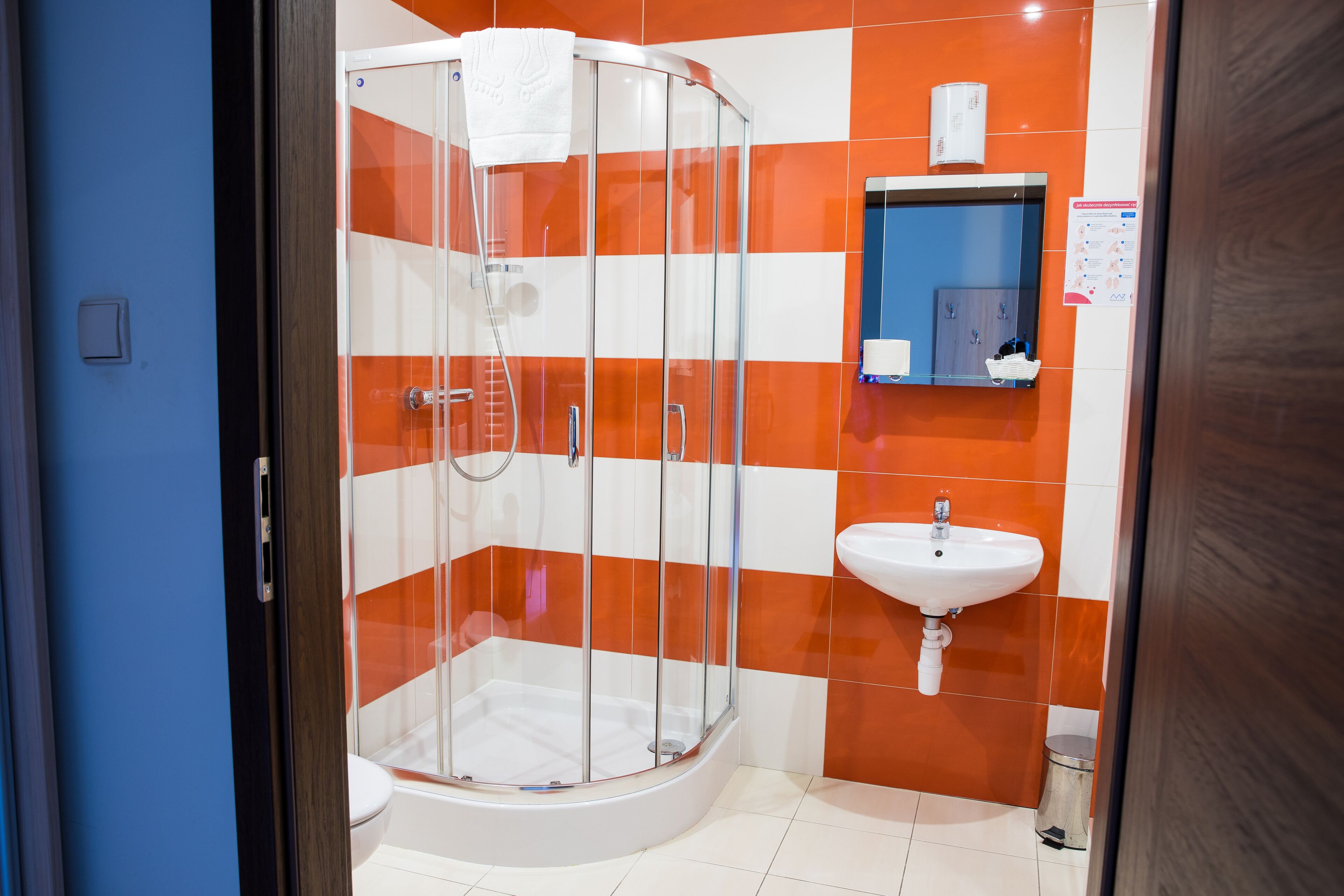 Un bany amb dutxa de vidre, un lavabo blanc i rajoles taronja i blanques.