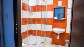 Un bany amb dutxa de vidre, un lavabo blanc i rajoles taronja i blanques.