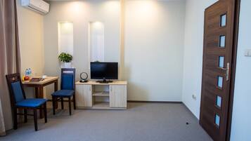 A small, neatly arranged room with a desk, two chairs, a television, and a door.