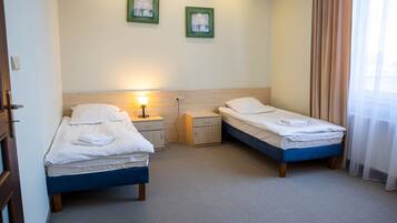 Une chambre d’hôtel avec deux lits simples, une table de chevet, une lampe fixée au mur et deux tableaux encadrés.