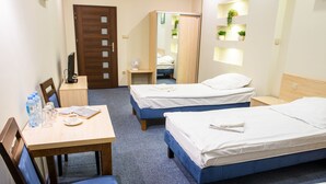A hotel room with two single beds, a wooden desk with a chair, a small table with a fan, and a wardrobe. - Hotel Kardamon (Tarnow)