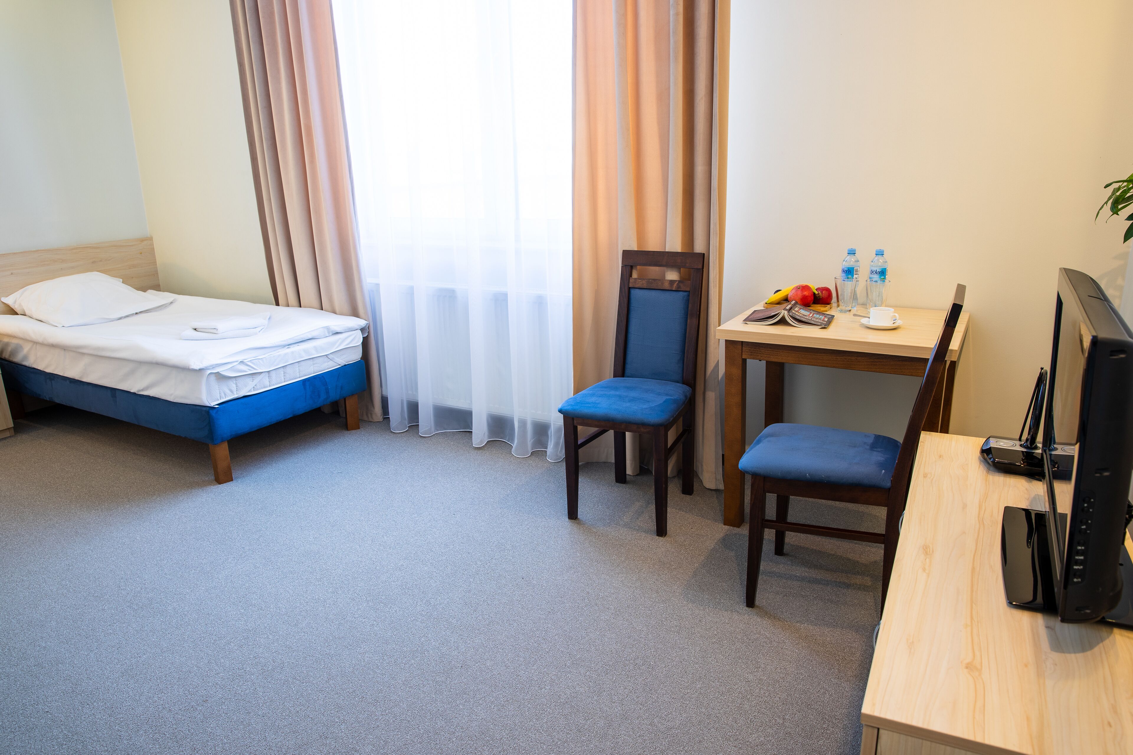 Een hotelkamer met een bed, een bureau met stoel, een televisie en een raam met gordijnen.