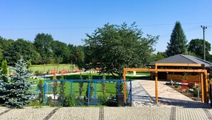 A covered outdoor seating area with a wooden structure and a metal roof, surrounded by a blue fence and greenery. - Hotel Kardamon (Tarnow)
