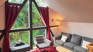 A cozy room with a large window, a grey sofa, a grey armchair, a wooden coffee table, and a red rug. - Experience with us the Harz im Glück! Vacation for two in Wernigerode! (Wernigerode)
