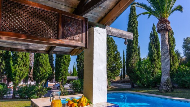 Área junto à piscina com um bar, uma cesta de frutas e uma piscina azul cristalina.