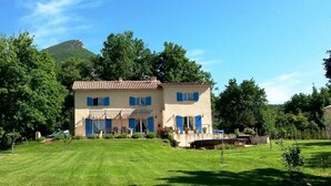 Une maison à deux étages dotée d’un balcon, entourée d’une pelouse bien entretenue et d’arbres.