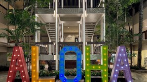 Illuminated letters spelling "ALOHA" in a courtyard with a modern building in the background.
