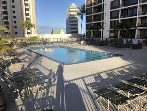 A swimming pool with lounge chairs and palm trees, surrounded by tall buildings.