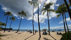 A beach with palm trees, sun loungers, and umbrellas under a clear sky.