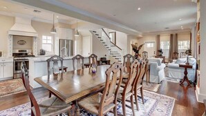Une cuisine spacieuse avec un grand îlot central, une table à manger en bois et des chaises. Un escalier mène à un autre niveau.