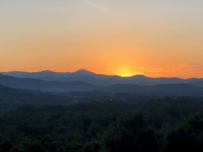 A sunset over a range of mountains with a forested valley in the foreground. - Pisgah View Cabin - Year round Mountain View  - Convenient location (Hendersonville)