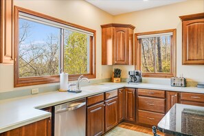 A kitchen with wooden cabinets, a white countertop, a dishwasher, and a window with a view of trees.