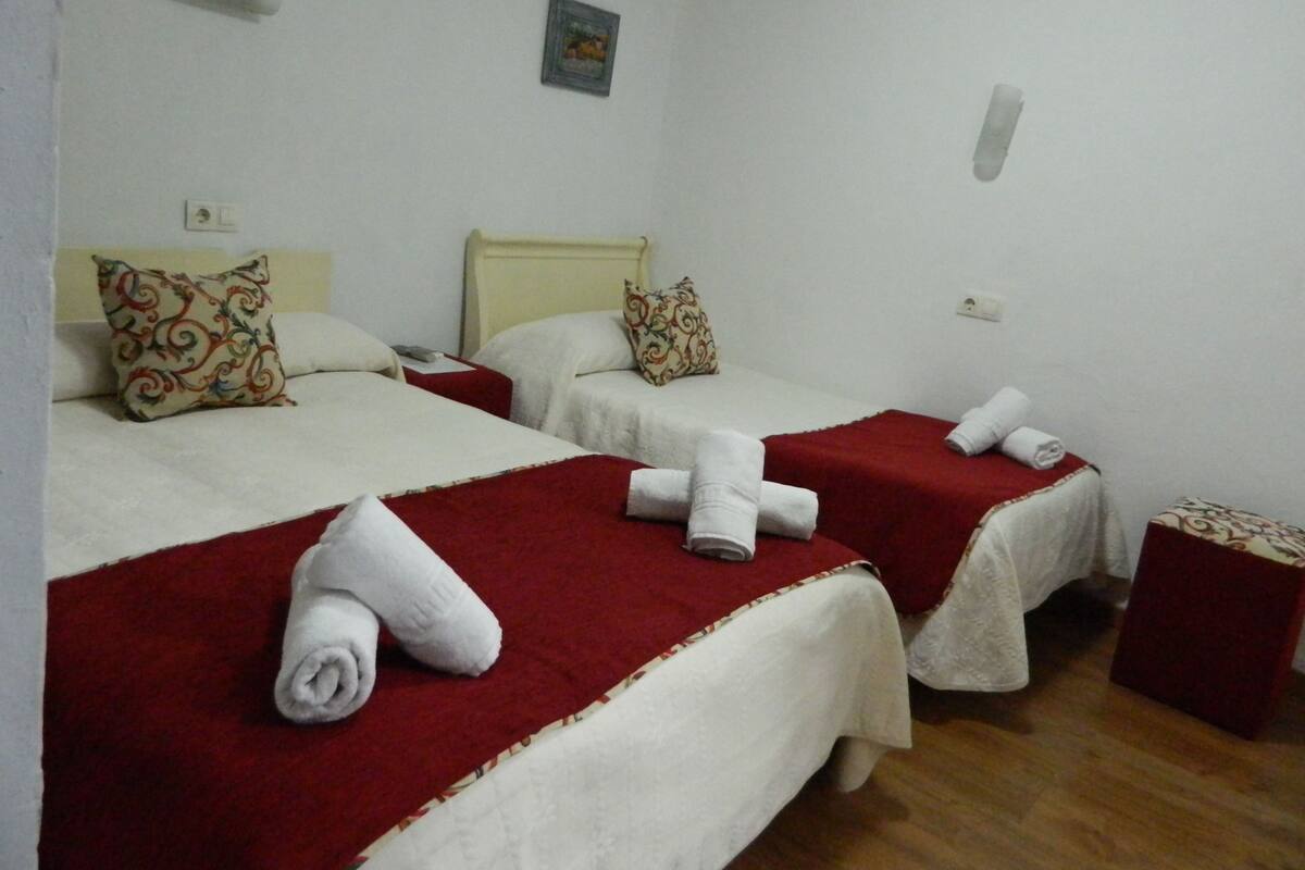 Habitació d'hotel amb dos llits, cadascun amb llençol vermell i roba de llit blanca, una petita taula de nit i una làmpada fixada a la paret.
