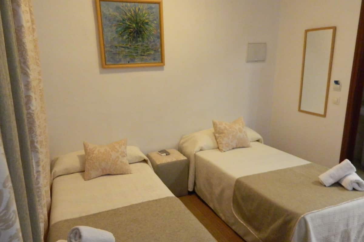 Habitació d'hotel amb dos llits, cadascun amb un coixí i una manta, una tauleta de nit amb un telèfon, un quadre a la paret i un mirall.