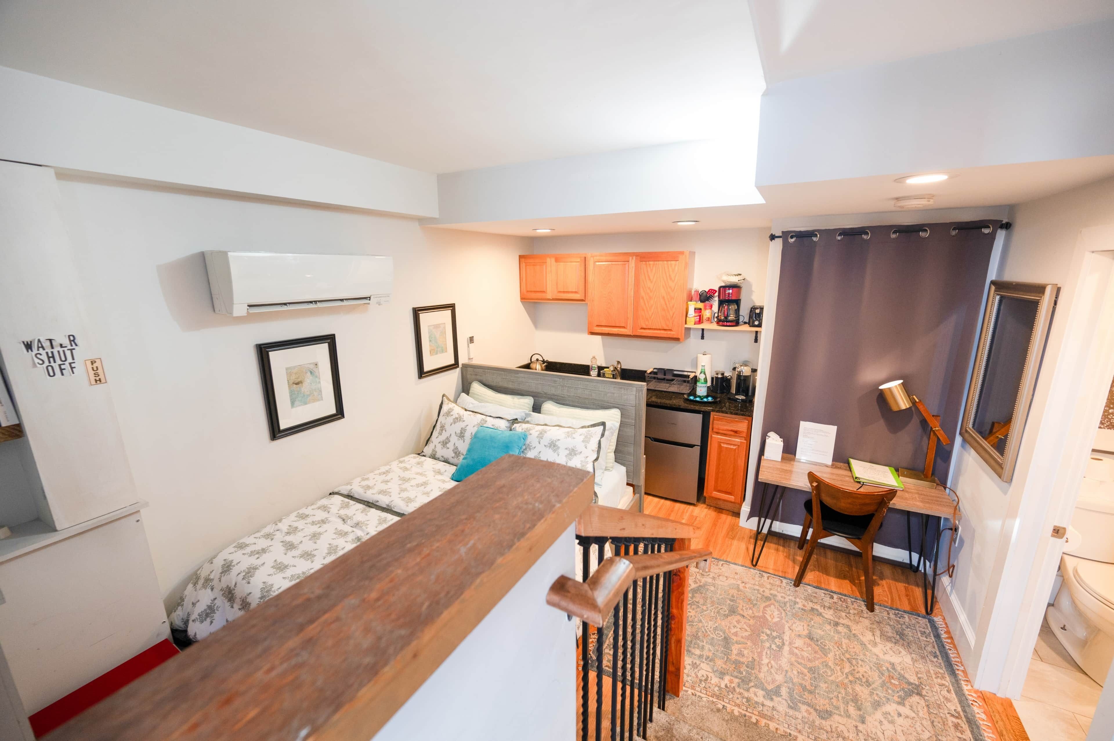 A compact living space with a kitchenette, a bed with patterned bedding, a dining area with a chair, and a small table.
