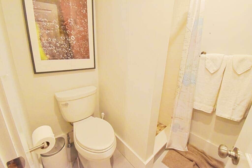 Ein Badezimmer mit Toilette, Toilettenpapier, einem Handtuchhalter mit Handtüchern und einer Duschvorhang.