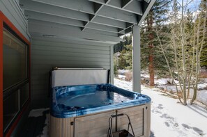 Un bain  à remous installé sous une véranda, offrant une vue sur un paysage enneigé et des arbres.
