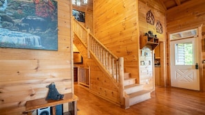 A wooden interior with a staircase, a painting of a waterfall, and a door with a geometric design. - 4BR cabin with hot tub, game room, fire pit, and mountain views. (Sautee Nacoochee)