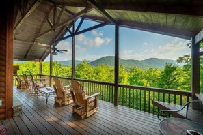 A wooden deck with outdoor furniture, a ceiling fan, and a view of green mountains.