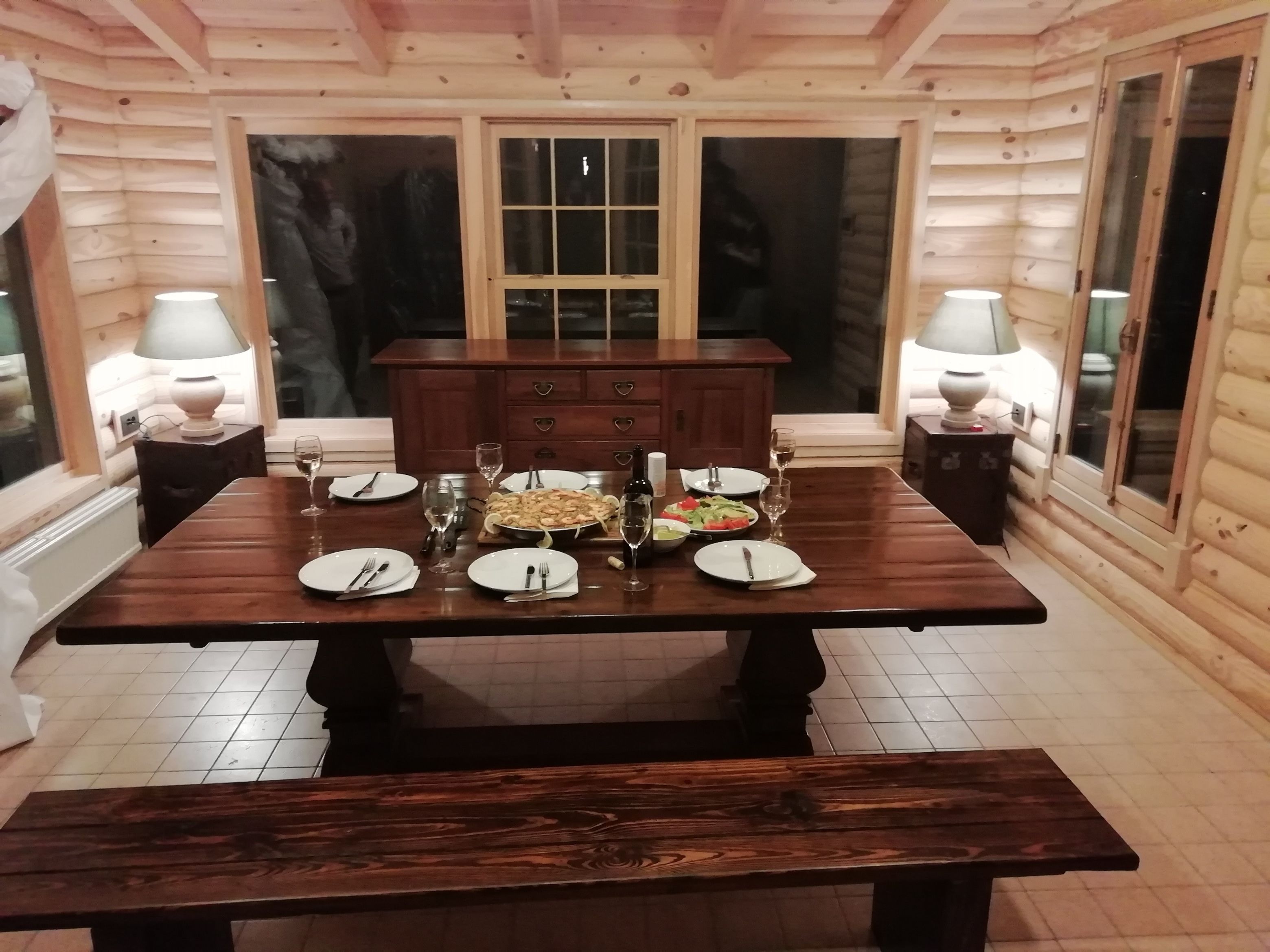 Een houten eettafel gedekt met borden, bestek, glazen en een gerecht in het midden.