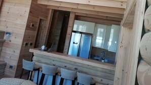 A wooden interior with a kitchen area, a dining table with chairs, and a high ceiling with exposed beams. - Chalet de Charme (Al Arz)